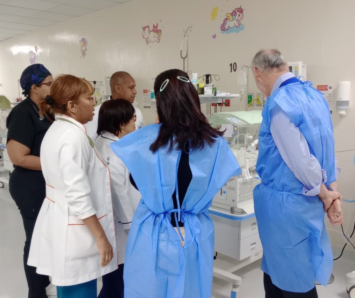 Profesionales de la salud y de OPS alrededor de una incubadora observando a un recién nacido.