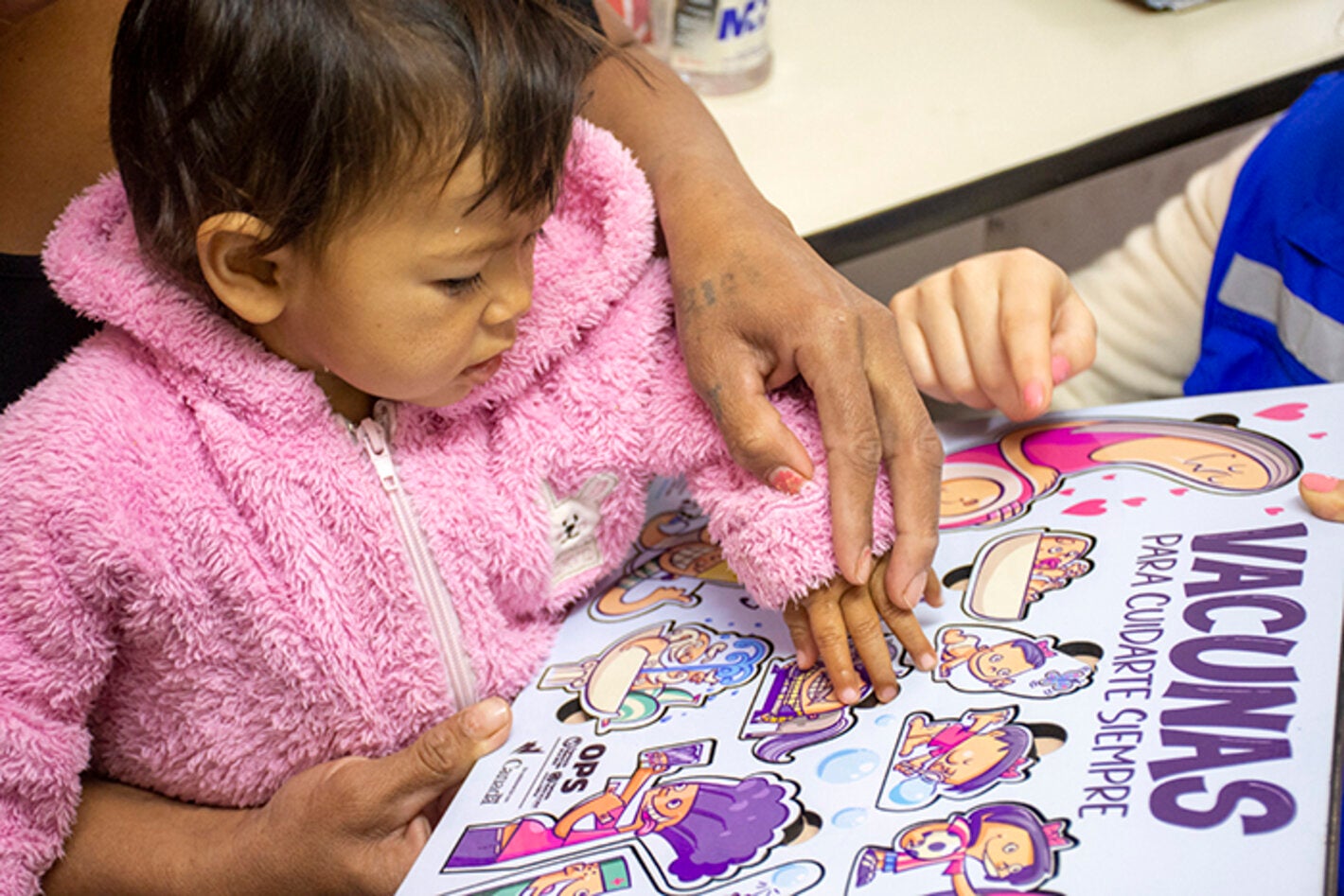 Foto de niña con su mamá a la espera de ser vacuna mientras juega con un rompecabezas sobre vacunas