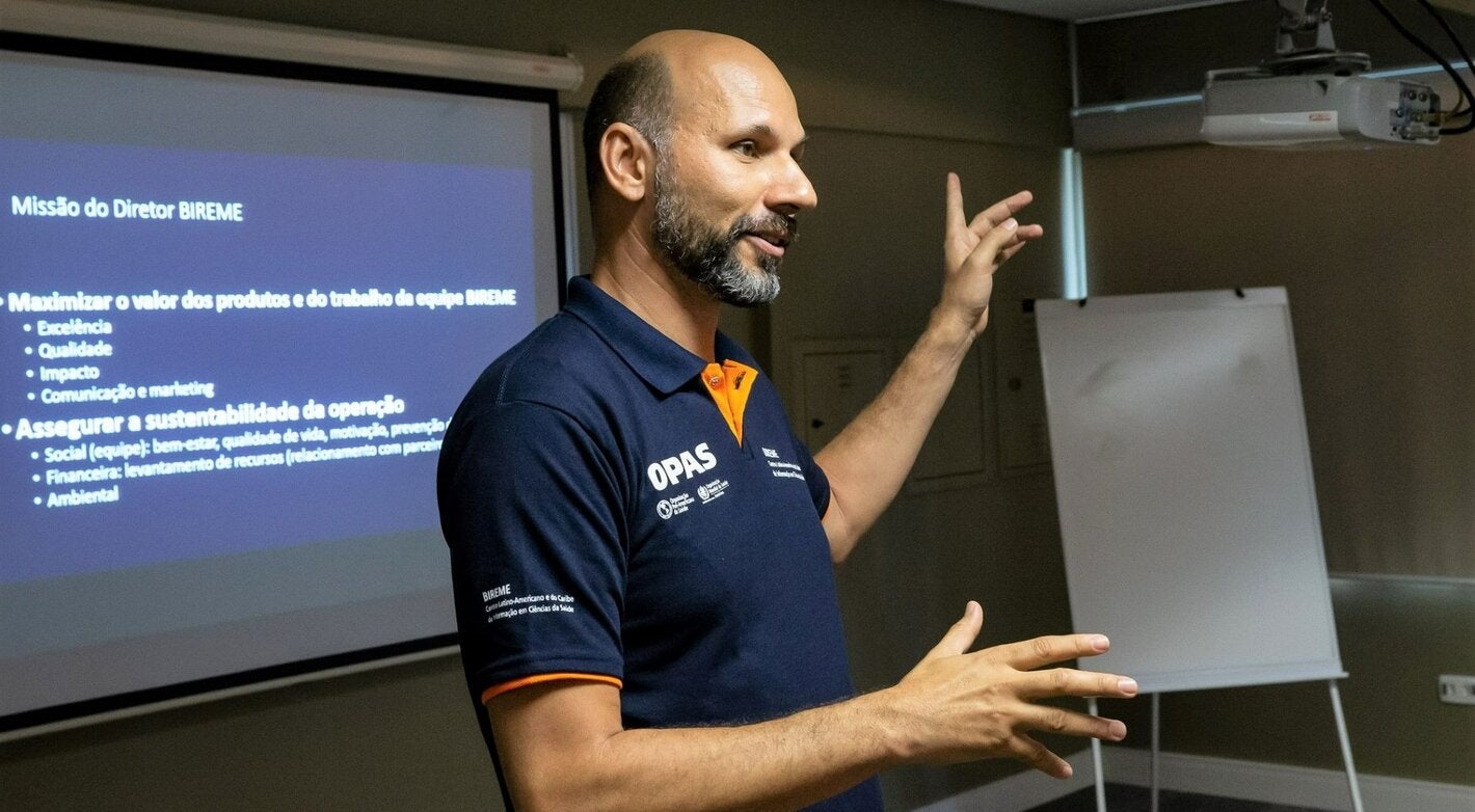 Uma foto de João Paulo Souza, Diretor da BIREME, vestindo uma camisa da OPAS, falando e gesticulando em uma palestra.
