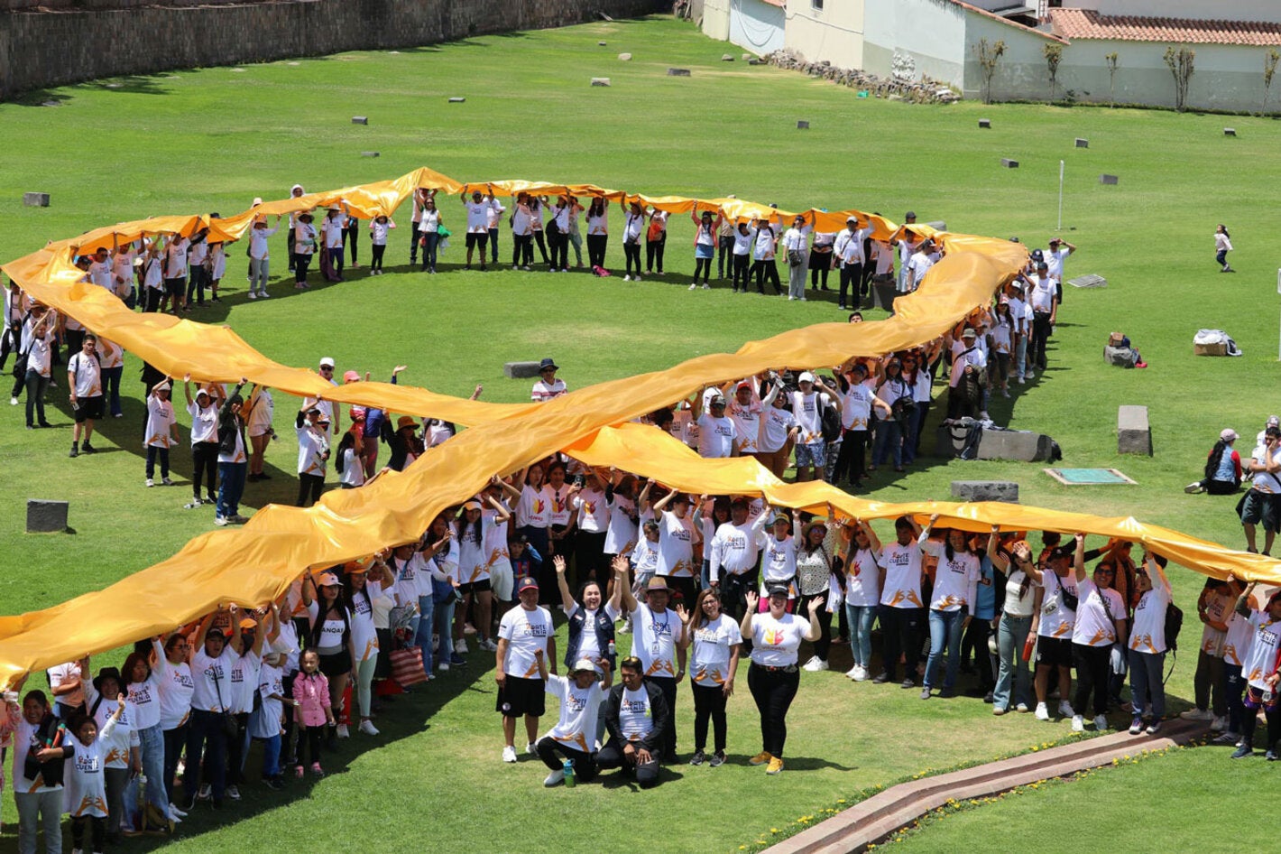 Personas en un campo amplio sosteniendo el emblema del cáncer infantil (lazo dorado)