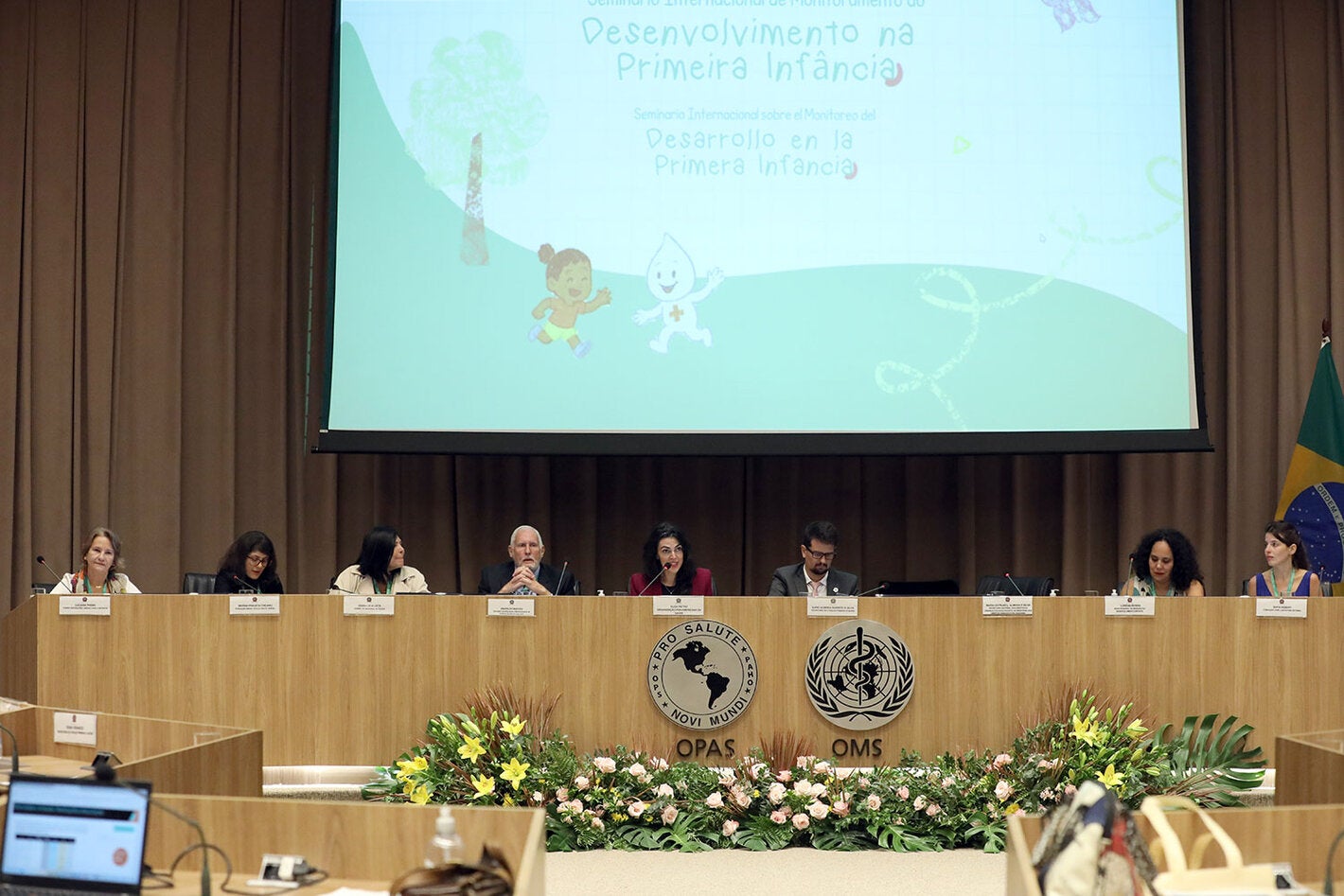 Mesa de abertura do evento com oito pessoas e um telão ao fundo escrito "Desenvolvimento na primeira infância"