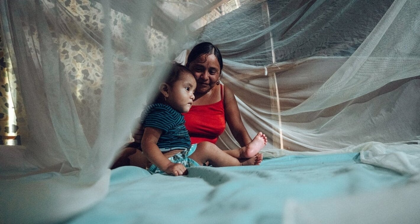 Mother and child under mosquito net over bed
