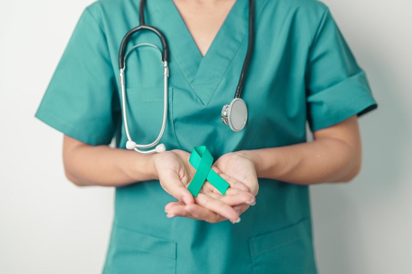 A female doctor with a teal shirt holds a teal ribbong in her hands. The human figure appears from the shoulders to the waist, as the hands are the important element in the picture