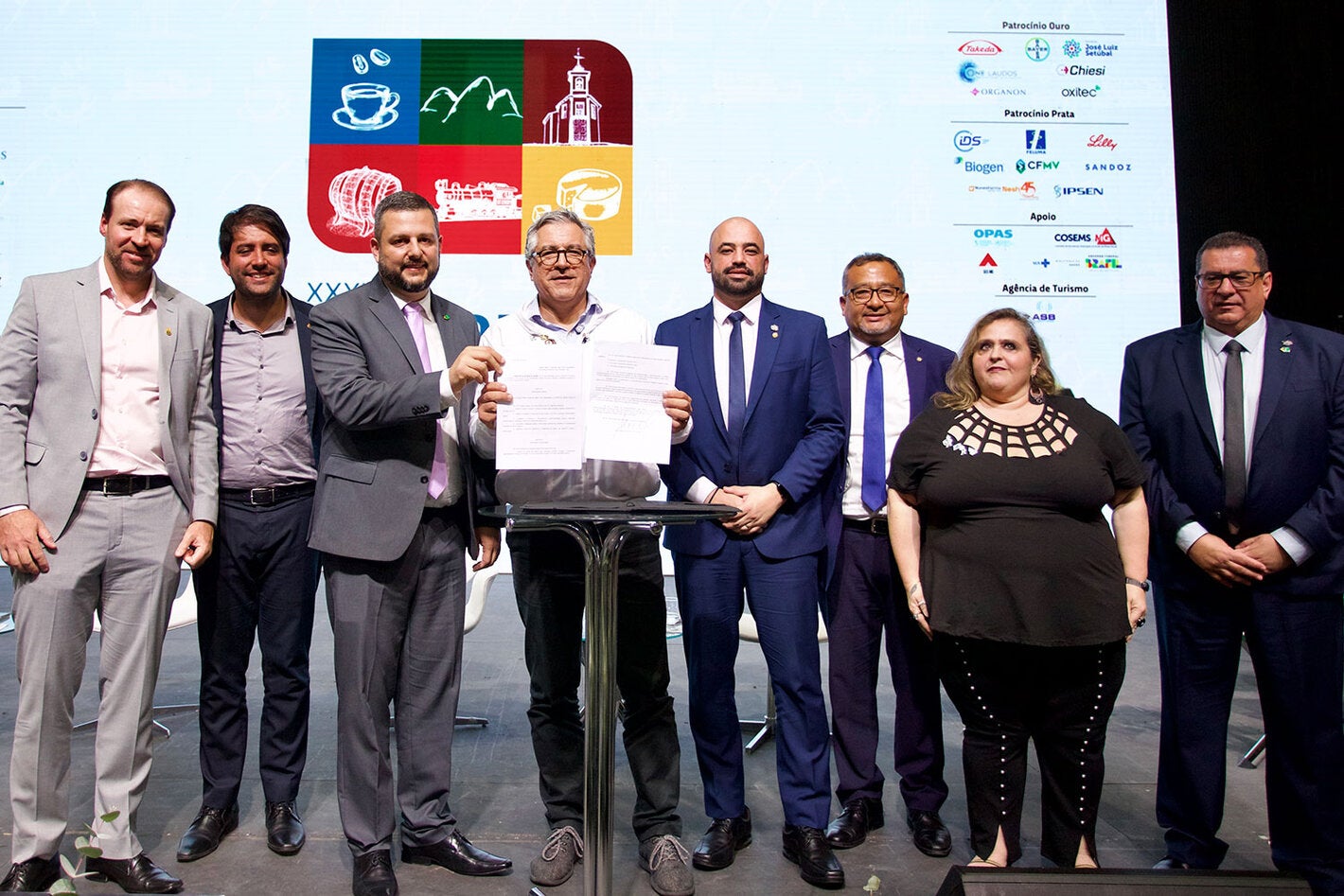 O Ministro da Saúde do Brasil, Alexandre Padilha, segura documentos assinados por ele. Na foto, ao lado dele estão o presidente do Conasems e outras autoridades.