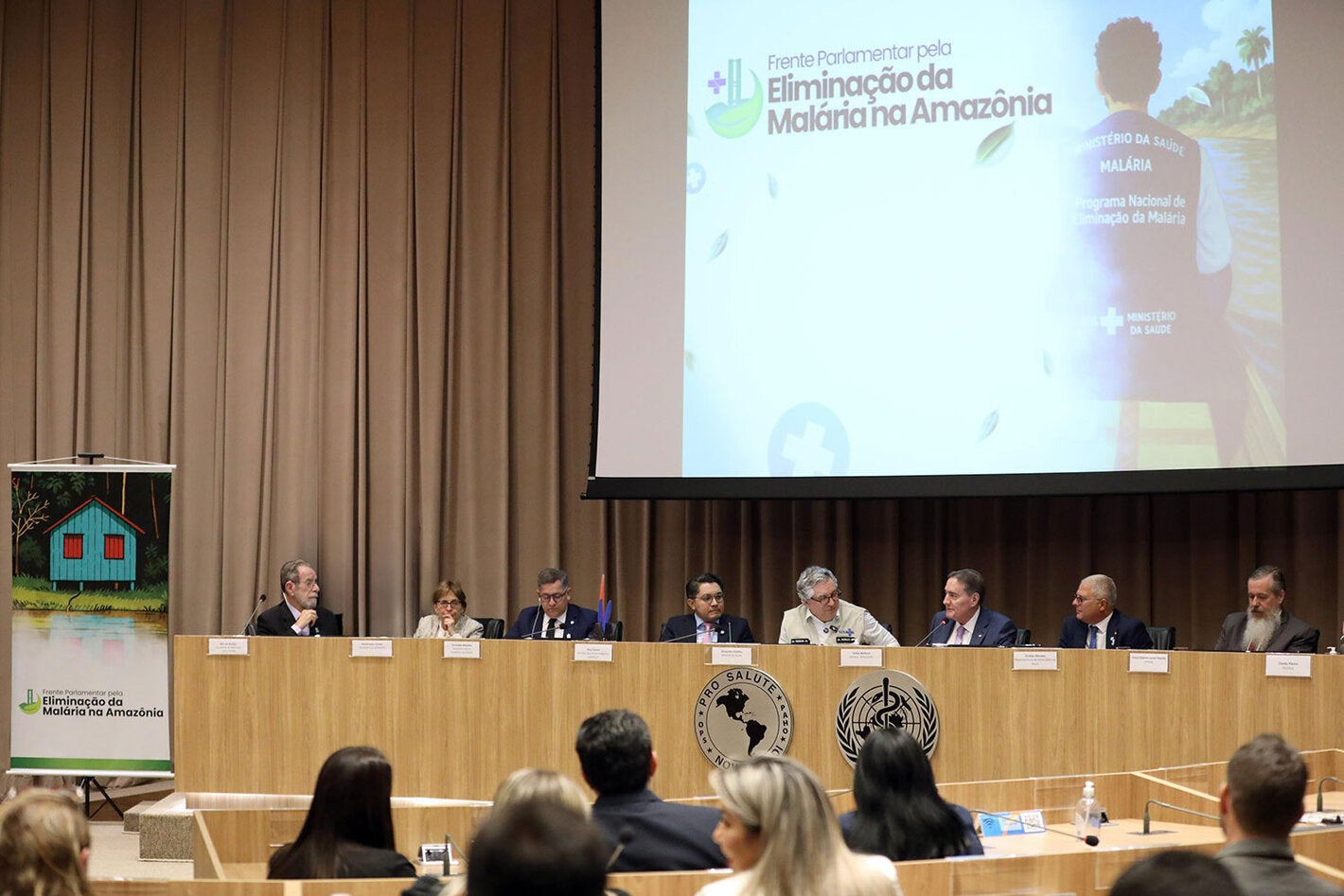 Mesa de abertura do evento com telão ao fundo com a inscrição "Frente Parlamentar pela Eliminação da Malária na Amazônia"