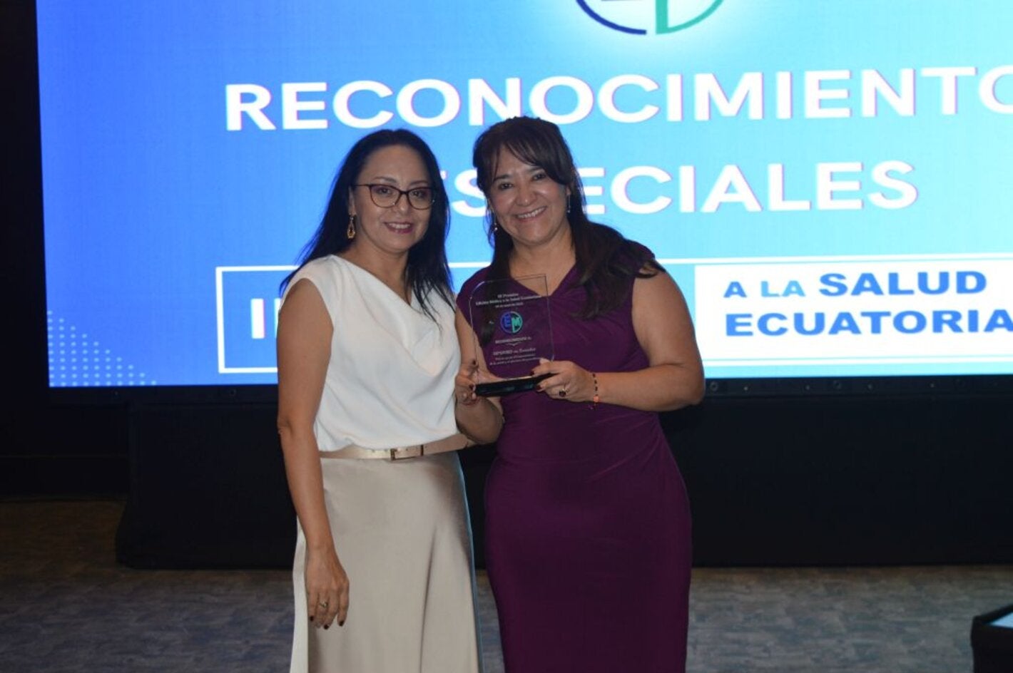 La representante de la OPS/OMS en Ecuador, Dra. Sonia Quezada, recibe de la periodista Cristina Coello, el reconocimiento entregado a la oficina de parte de Edición Médica.
