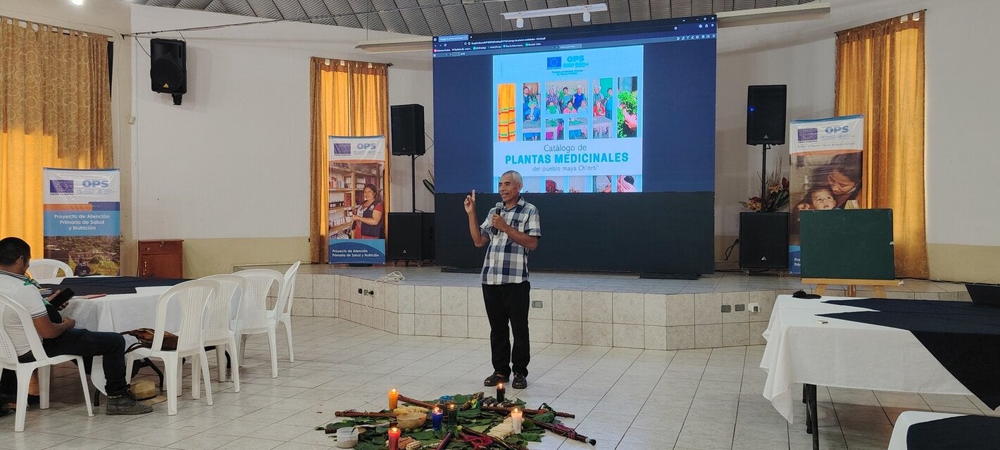 Un hombre frente a una pantalla luminosa, presenta el catálogo de plantas medicinales del pueblo maya Ch'orti'