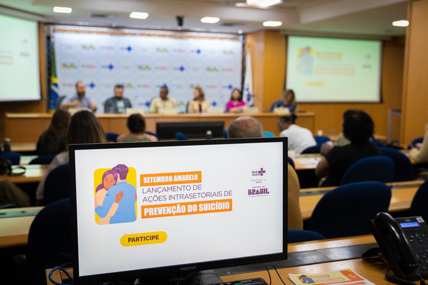 logomarca do evento, ao fundo mesa de palestrantes