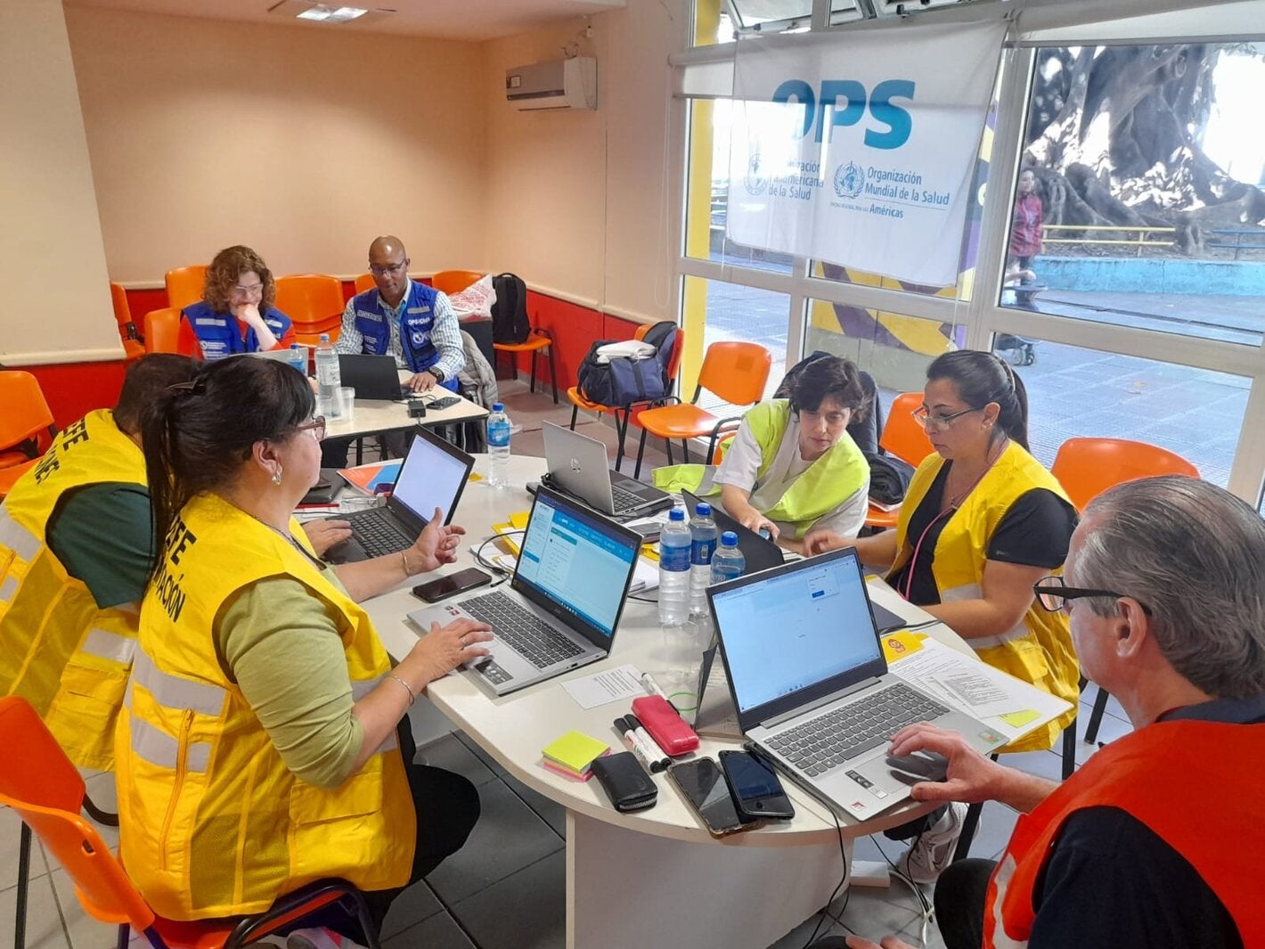participantes de taller con chalecos amarillos, sentados alrededor de una mesa con laptops