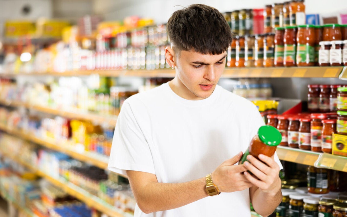 Un hombre joven leyendo la etiqueta frontal del producto (salsa)