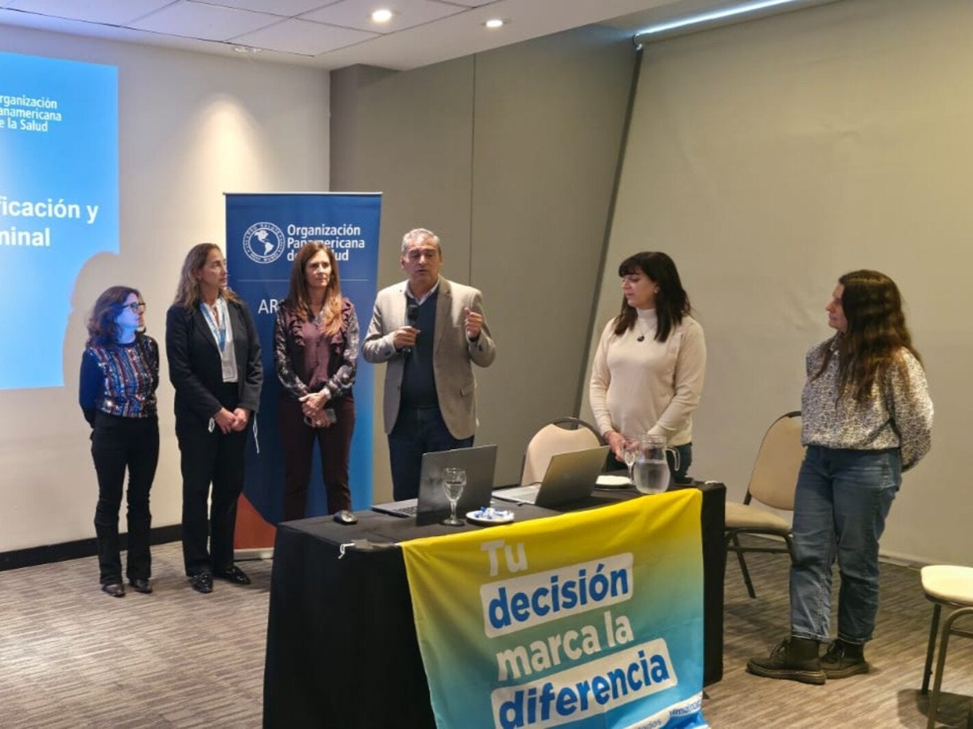 Autoridades dan inicio a la jornada. En la mesa de disertantes, una bandera dice "Tu decisión marca la diferencia"