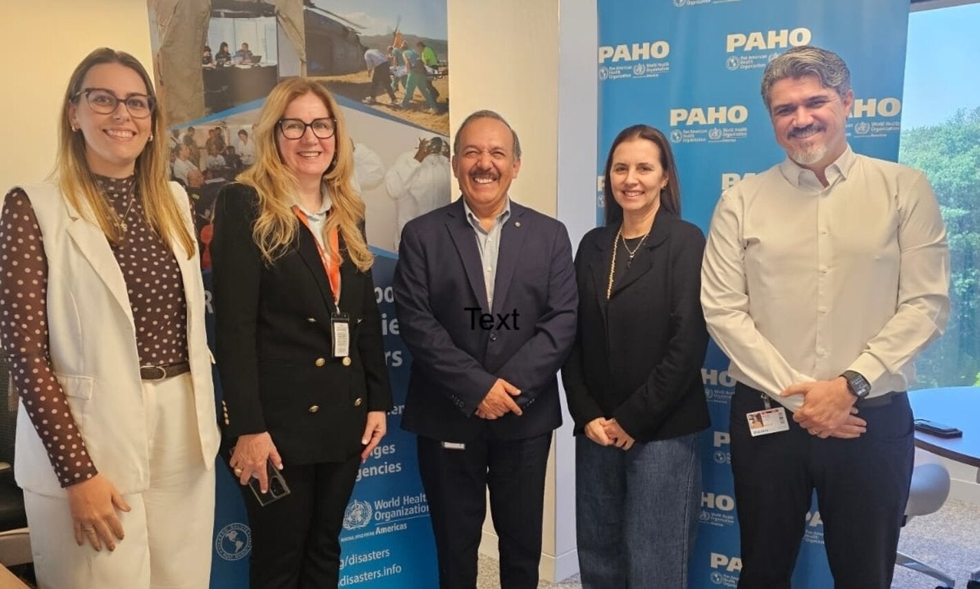 Delegación de salud de São Paulo y equipo de la OPS/OMS posan en el Centro de Operaciones de Emergencia, junto a un banner sobre respuesta a emergencias sanitarias.