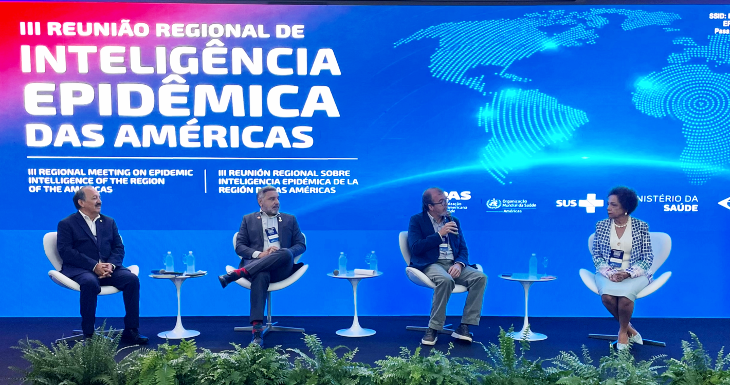 Panelistas sentados con fondo alusivo al evento, mostrando mapa mundi y título del evento