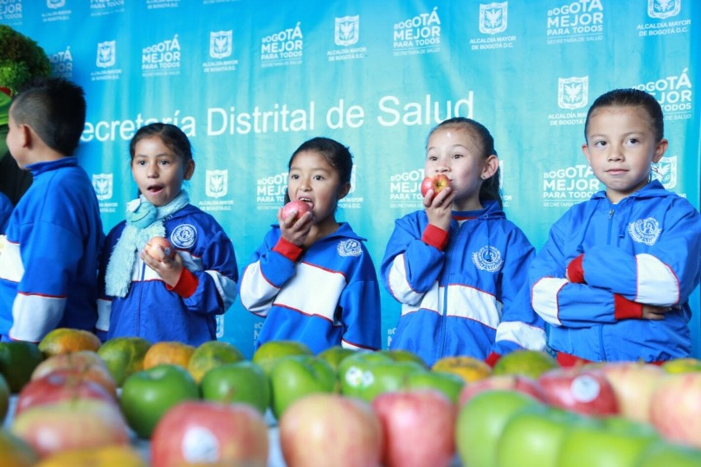 Niños y niñas vestidos con uniforme escolar deportivo, comiendo unas manzanas