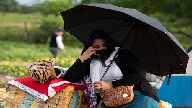 Una mujer migrante sentada bajo un paraguas.