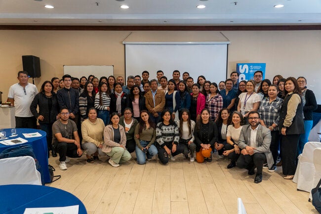 Grupo de aproximadamente 40 participantes del entrenamiento de la encuesta STEPS en Quito, Ecuador (8–10 de septiembre de 2025), posando para una foto en una sala de conferencias frente a una pantalla de proyección, con mesas y sillas visibles en los bordes.