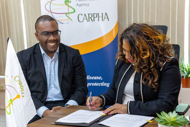 Photo Caption: (L-R) Dr. Horace Cox, CARPHA Director watches on as Dr. Lisa Indar, Executive Director signs the Framework Agreement  