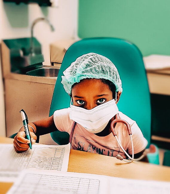 Masked girl with a medical hat, writing a form while seated on an chemotherapy armchair and looking straigth to the camera
