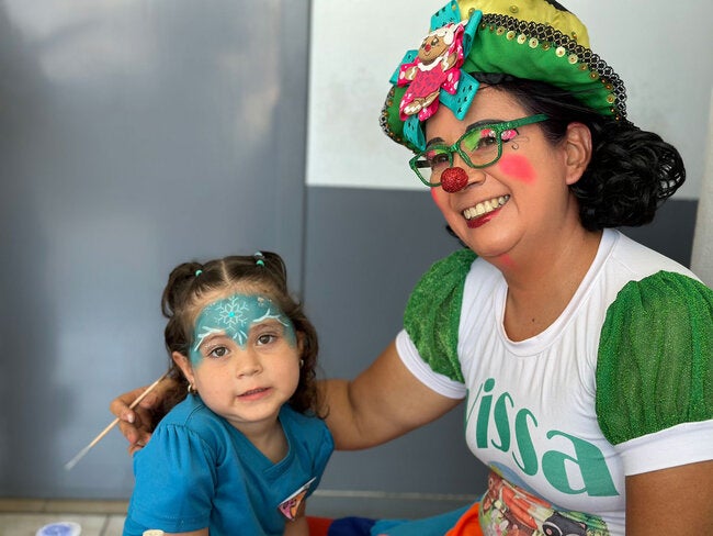 En la clínica del Seguro Social de Aguas Zarcas, una payasita pinta caritas y hace figuras con globos, mientras los niños salen del área de vacunación.