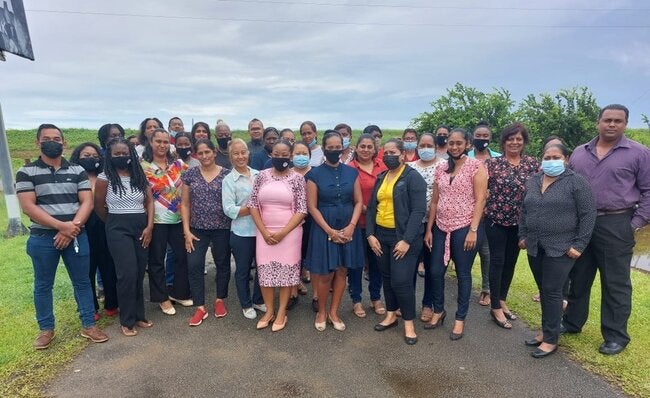 A group of people standing on an open space for a group photo, some of them with mask, other smiling