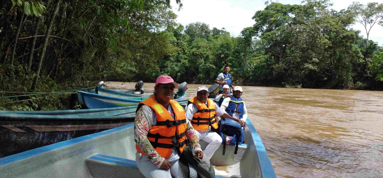 Personas en un bote de madera en la orilla de un río. Las personas tienen chalecos salvavidas.