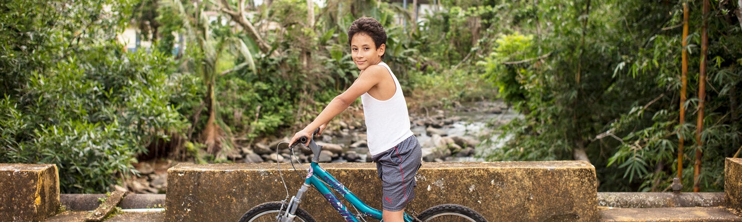 niño montando su bicicleta con árboles en el fondo