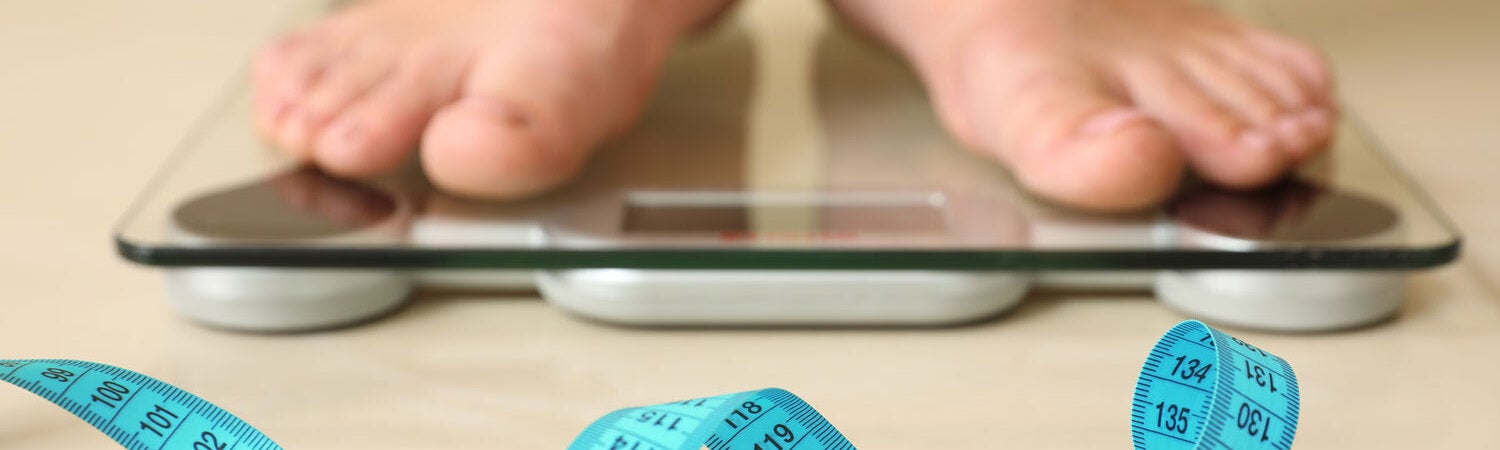 Photo of a blue measuring tape in the front and an electronic weight bascule with a pair of feet over it