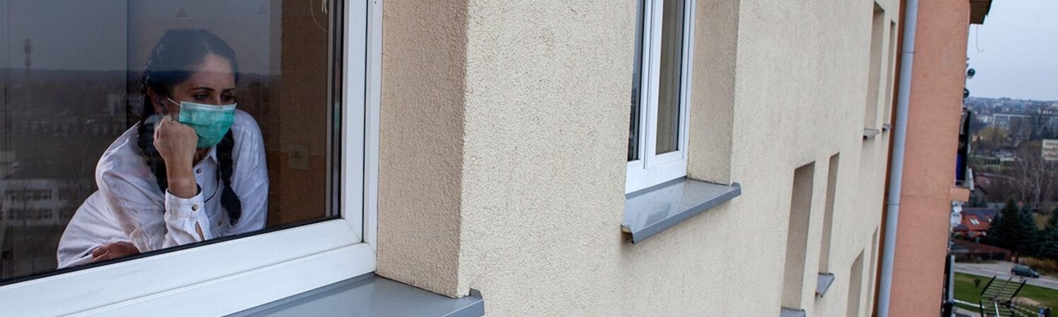 Mujercon mascarilla mirando por la ventana hacia la calle