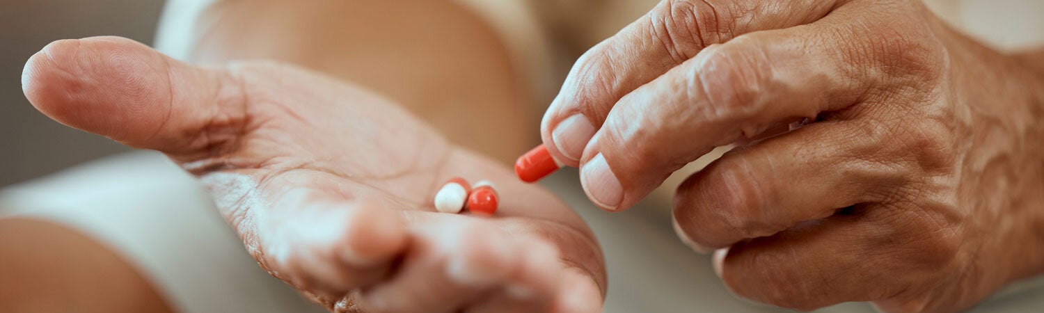 Elderly patient with pills in hand/Credit/PeopleImages
