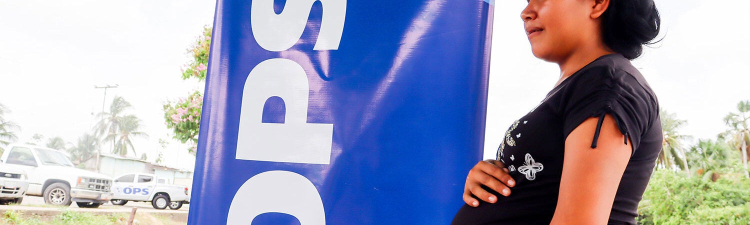 Mujer embarazada parada a la par de un rótulo de OPS/OMS