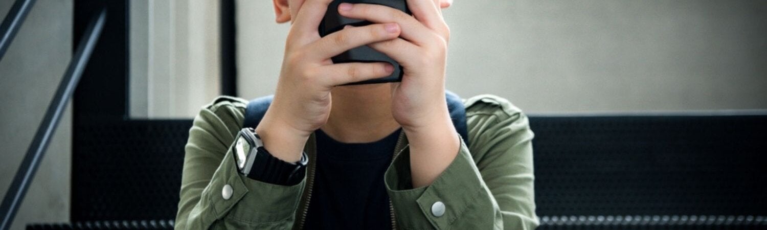 A kid seating on the couch using his mobile phone