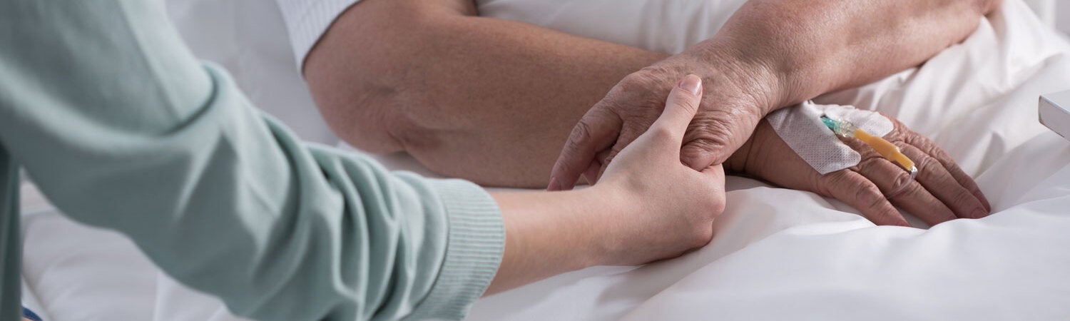 Image showing the hand of a healthcare worker holding the hand of a patient lying on a hospital bed